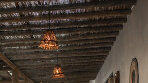Un espace extérieur abrité, doté d’un sol en béton, d’un escalier en bois menant à une porte et de luminaires suspendus.