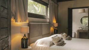 Une chambre à coucher avec un lit, deux lampes de chevet, une fenêtre avec des rideaux, un miroir rond et une petite table avec une lampe.