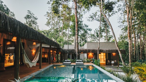 Un espace aménagé au bord de la piscine, doté d’une structure à toit de chaume, de sièges et offrant une vue sur les arbres environnants.
