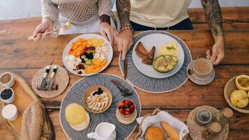 Ein Holztisch mit Tellern voller Speisen, darunter Obst, Nüsse und Brot, sowie eine Kaffeetasse.