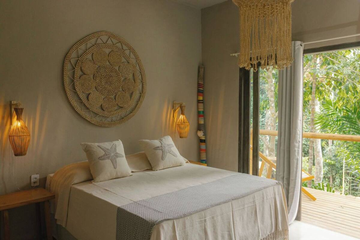 A bedroom with a bed, a wall hanging, and a view of greenery.