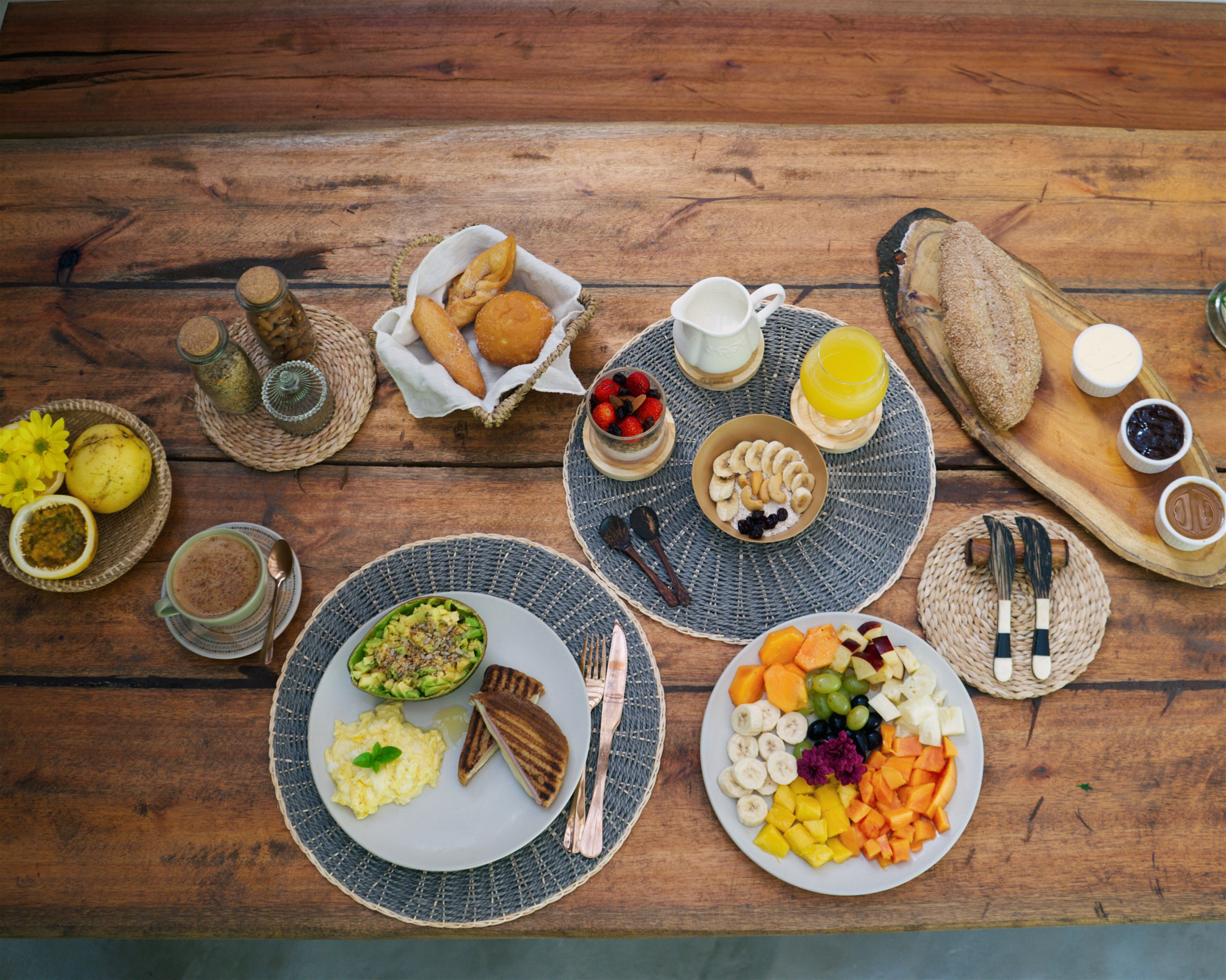 Et træbord med morgenmad, herunder æg, ristet brød, frugt og kager.
