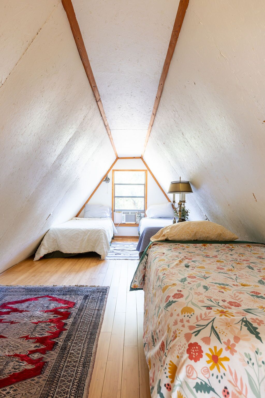 Una habitación tipo dormitorio con dos camas, una ventana, una lámpara y una alfombra.