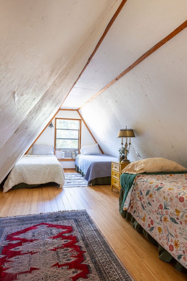 A bedroom with a sloped ceiling, a bed with a floral bedspread, a bedside table with a lamp, and a rug on the floor.