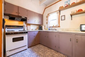 A kitchen with a stove, oven, cabinets, and a window. - The Library - A Hill Country Cottage (San Marcos)