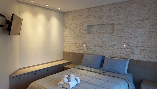 Een moderne slaapkamer met een stenen muur, een flatscreen televisie aan de muur, een bed met een gewatteerd dekbedovertrek en een nachtkastje met een lamp.