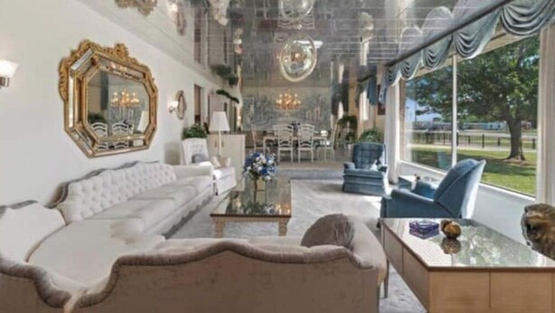 Uma sala de estar espaçosa com um sofá branco, uma poltrona azul e uma mesa de centro de vidro.