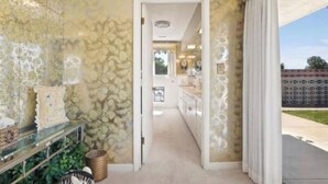 Corredor com paredes estampadas, uma vitrine de vidro e vista para uma área de cozinha.