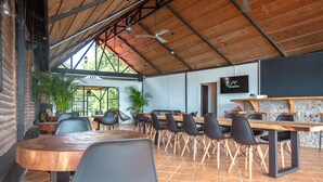 A spacious indoor dining area with high ceilings, wooden tables, and black chairs. - Buen Camino Hotel, San Mateo (San Mateo)