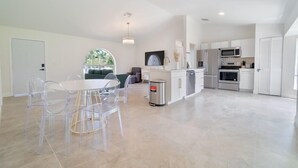 A modern kitchen with white cabinets, stainless steel appliances, and a dining area with clear chairs and a round table.
