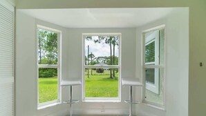 A corner room with three large windows, a white tiled floor, and two bar stools.