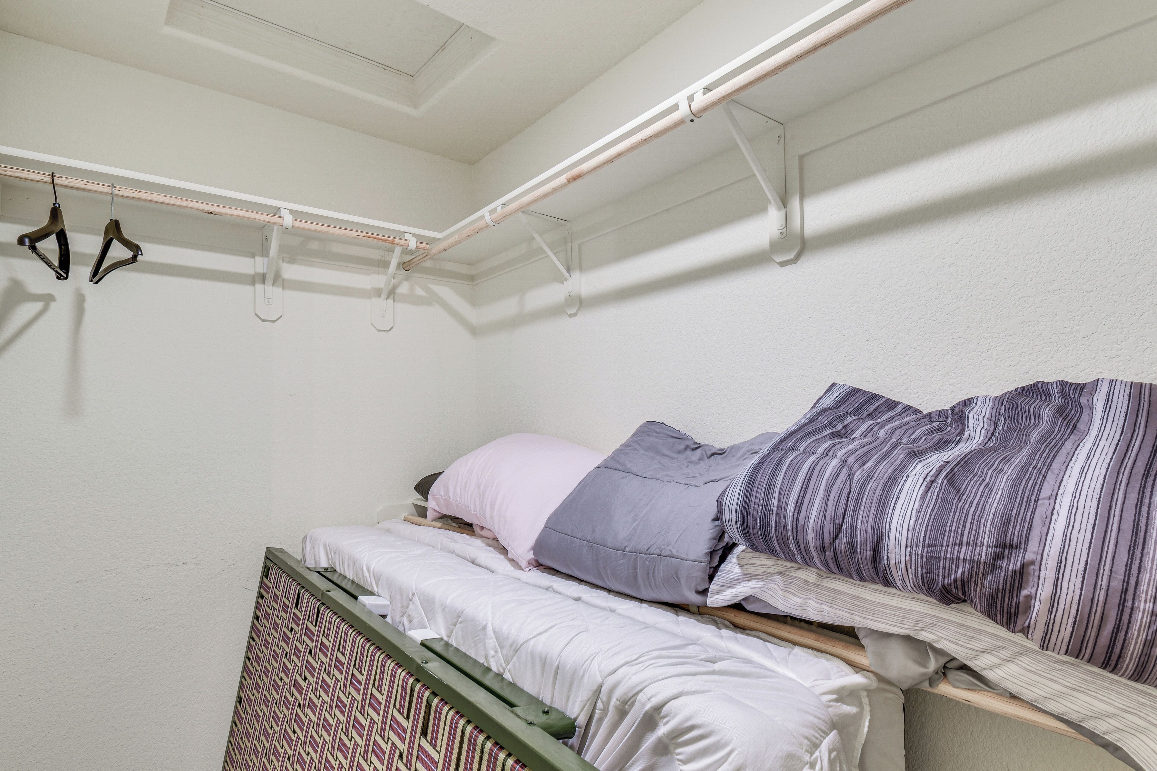 A small, single-bed room with a wooden headboard, a window with a view, and a clothes drying rack with hangers.