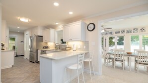 Una cocina moderna con armarios blancos, una isla central con taburetes, un refrigerador y un comedor con mesa y sillas.