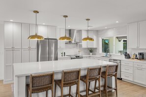A modern kitchen with white cabinets, a large island with bar stools, stainless steel appliances, and pendant lighting.