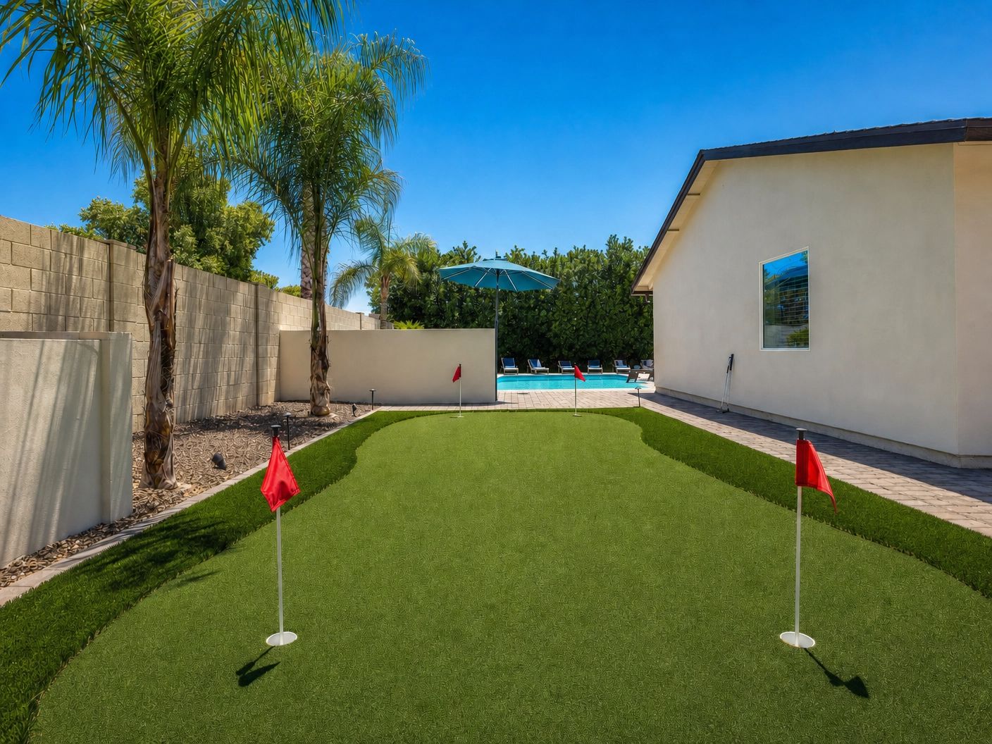 A backyard with artificial grass, a swimming pool, and a white building.