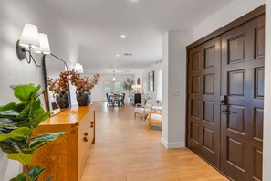 A hallway with a wooden reception desk, a dining area with a table and chairs, and a large dark wooden door.