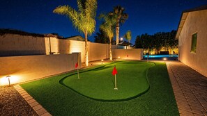 A nighttime golf course with artificial grass, palm trees, and a pool.