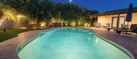 A swimming pool with a curved edge, surrounded by a landscaped garden and a building with outdoor seating.