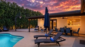 Ein Poolbereich mit Liegestühlen, einer überdachten Sitzgelegenheit und Blick auf den Sonnenuntergang.