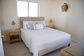 Un dormitorio con una cama, dos mesitas de noche, una ventana y un adorno en la pared.