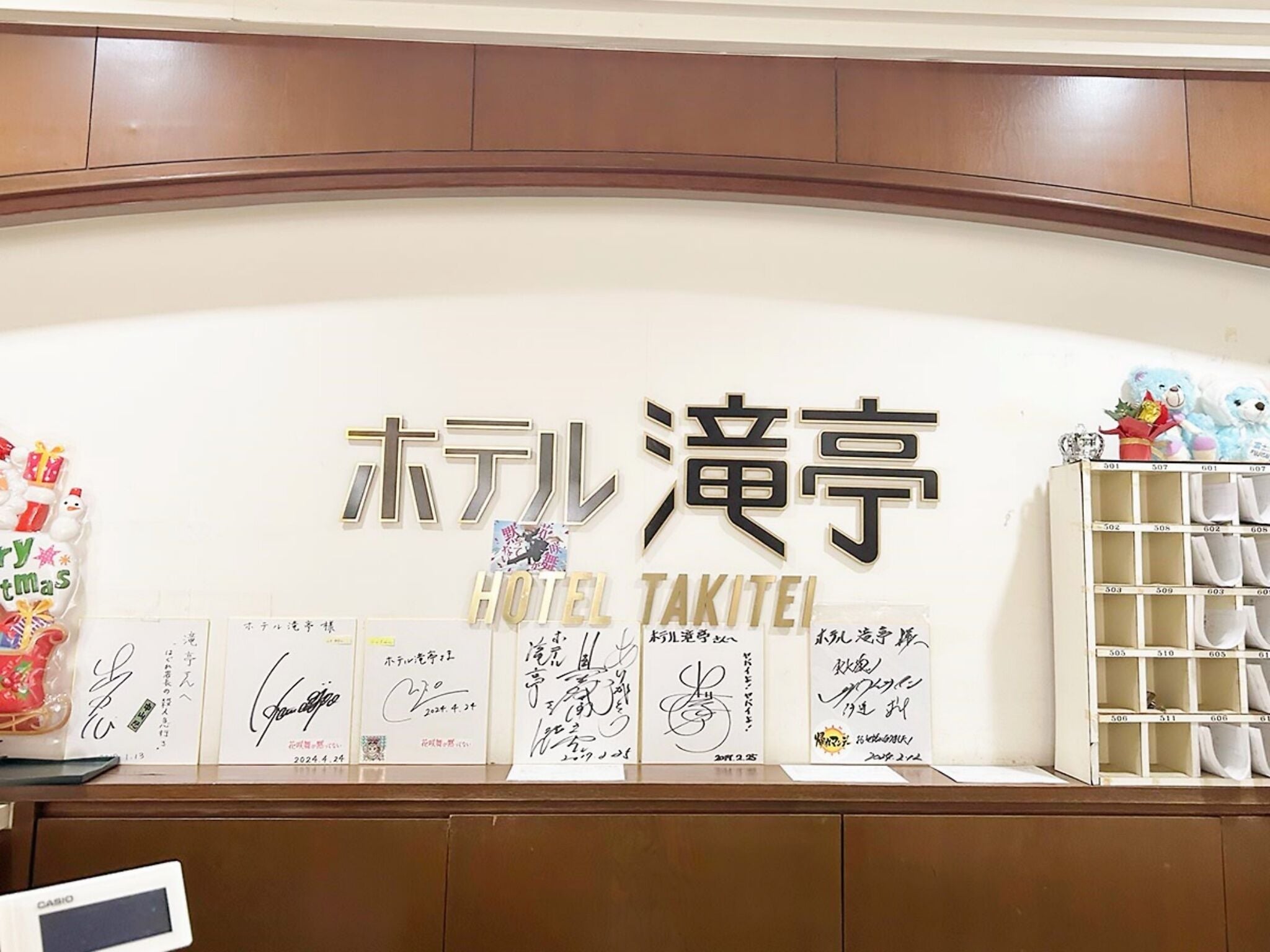 Un mostrador de recepción de hotel con un cartel que dice "HOTEL TAKITEI" y varios certificados o premios enmarcados.