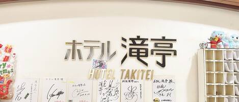 Un mostrador de recepción de hotel con un cartel que dice "HOTEL TAKITEI" y varios certificados o premios enmarcados.
