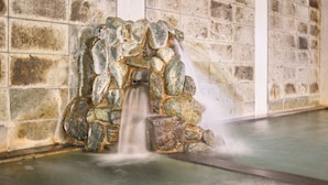 Een waterpartij van steen met een waterval in een betegelde ruimte.