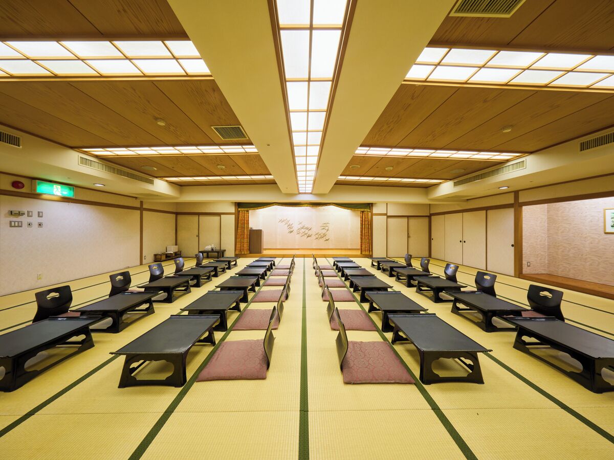 A conference room with rows of tables and chairs, a high ceiling with skylights, and a traditional Japanese tatami mat floor.