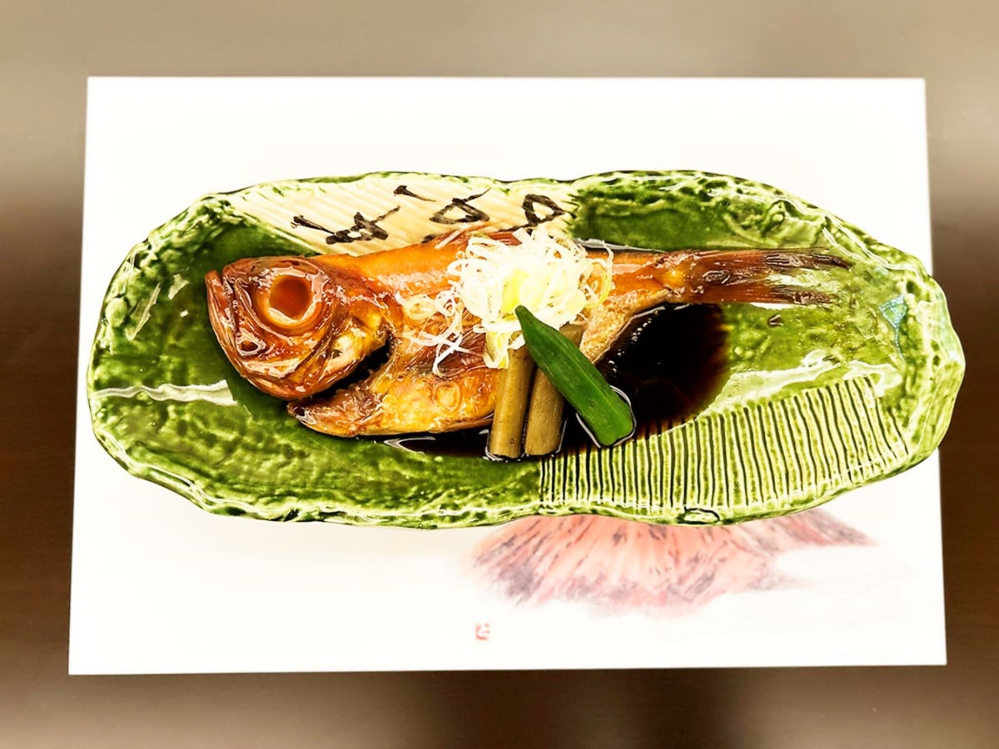 A fish dish on a green plate with a sauce and garnish.