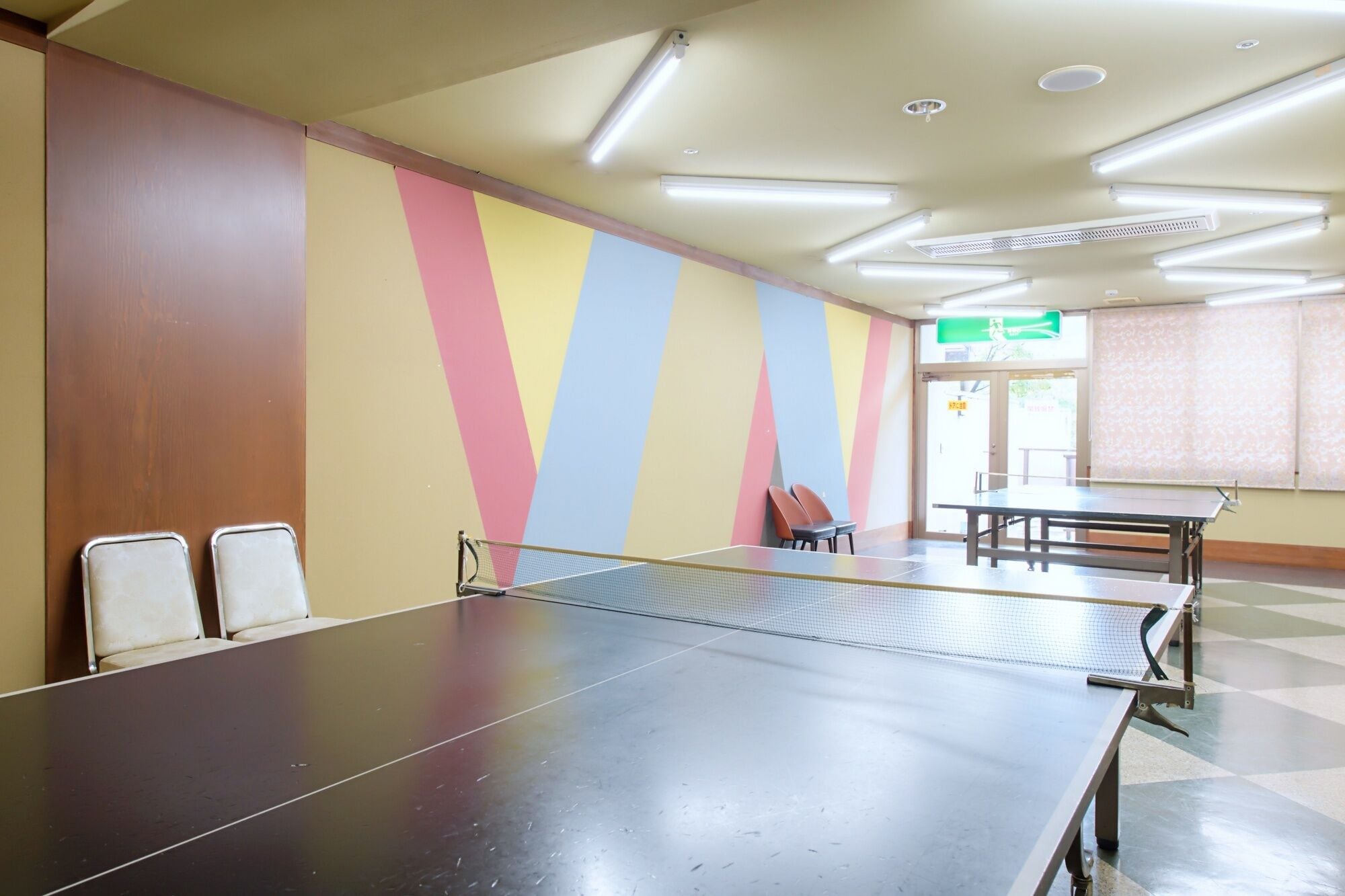 Una mesa de ping pong en una habitación con una pared colorida y una puerta al fondo.