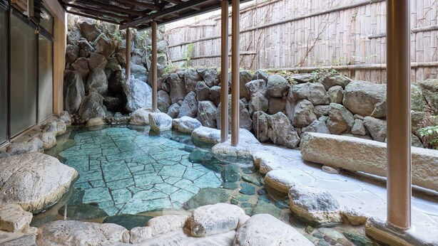 Een traditioneel Japans onsen met een stenen zwembad, omringd door rotsen en een houten hek.