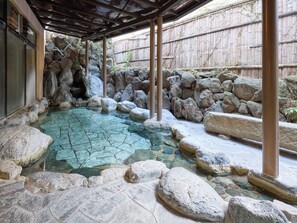Un onsen japonés tradicional con una piscina de piedra rodeada de rocas y una valla de madera.