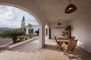 An open patio with a dining table and chairs, surrounded by arches and potted plants.