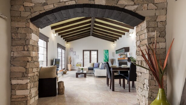 Amplia sala de estar con un arco de piedra, un sofá, una mesa de centro y una mesa de comedor con sillas.