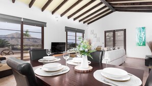 Comedor con una mesa de madera dispuesta para cuatro, ventanas amplias y vistas a montañas.