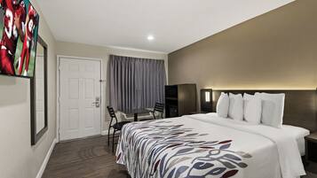 Quarto de hotel com cama, escrivaninha, cadeira, televisão e porta.