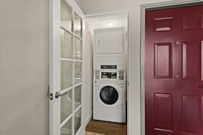 Un lavadero con lavadora y secadora, una puerta con paneles de vidrio esmerilado y una puerta roja.