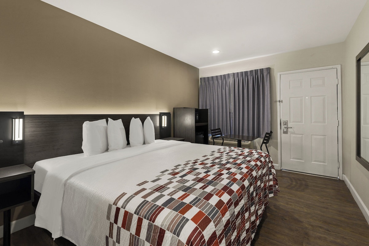 Habitación de hotel con una cama grande, un escritorio, una silla, un televisor y una puerta.