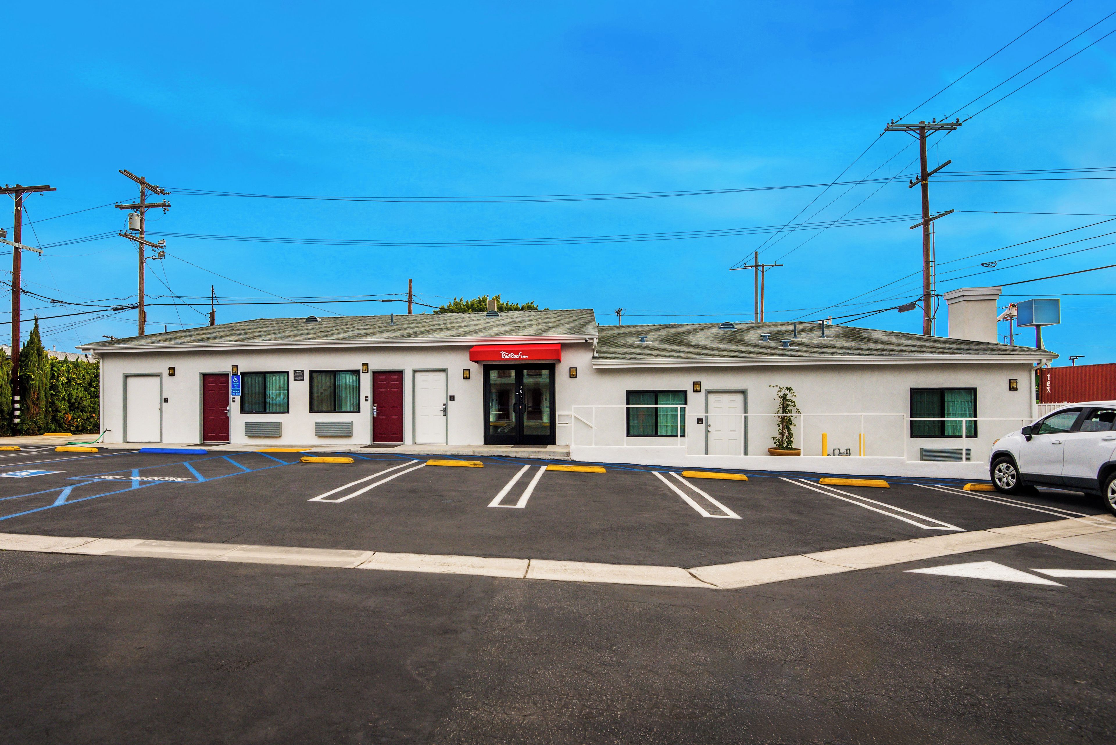 A motel with a red entrance, a parking lot with marked handicapped spaces, and a white car parked in the lot.