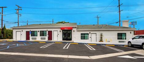 A motel with a red entrance, a parking lot with marked handicapped spaces, and a white car parked in the lot.