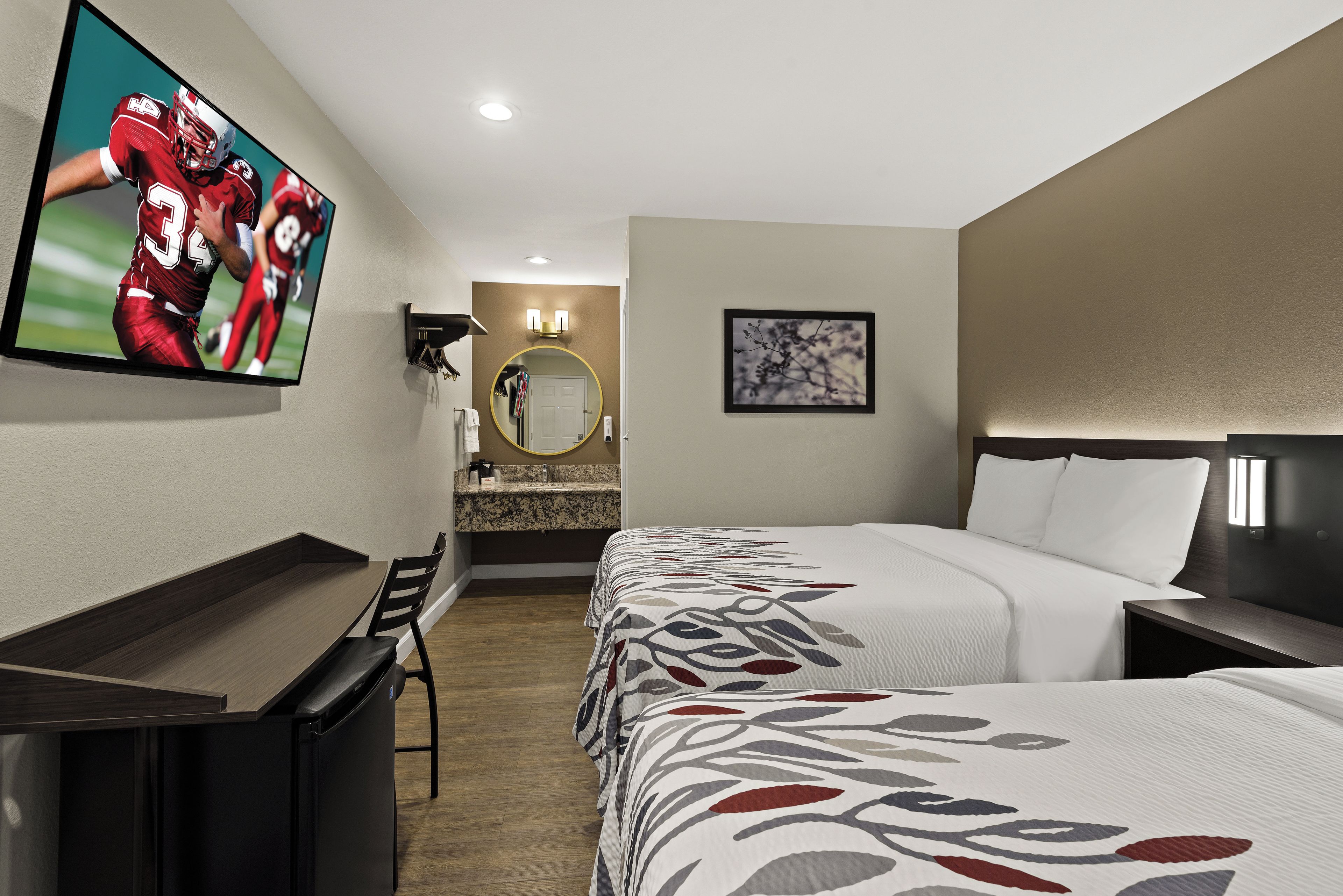 Een hotelkamer met een bed, een bureau, een televisie, een spiegel en een badkamer.