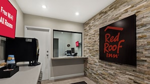 Un espace d’accueil avec une enseigne Red Roof Inn, une porte vitrée, un comptoir avec une machine à café et un panneau indiquant que le Wi-Fi est gratuit dans toutes les chambres.