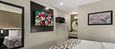 Ein Hotelzimmer mit einem großen Bett, einem an der Wand montierten Fernseher, einem Spiegel, einem Gemälde und einer kleinen Ablage mit Pflegeprodukten.