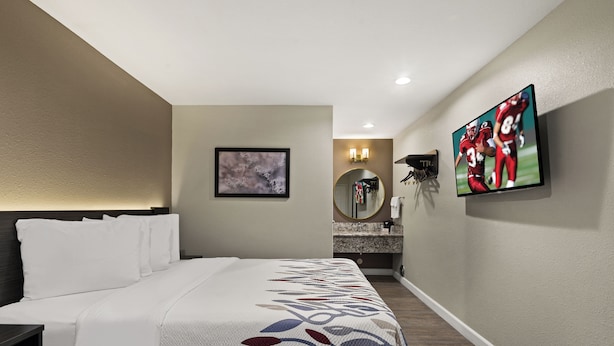 Une chambre d’hôtel comprenant un lit, un téléviseur fixé au mur, un miroir et une petite salle de bain avec un lavabo et des toilettes.
