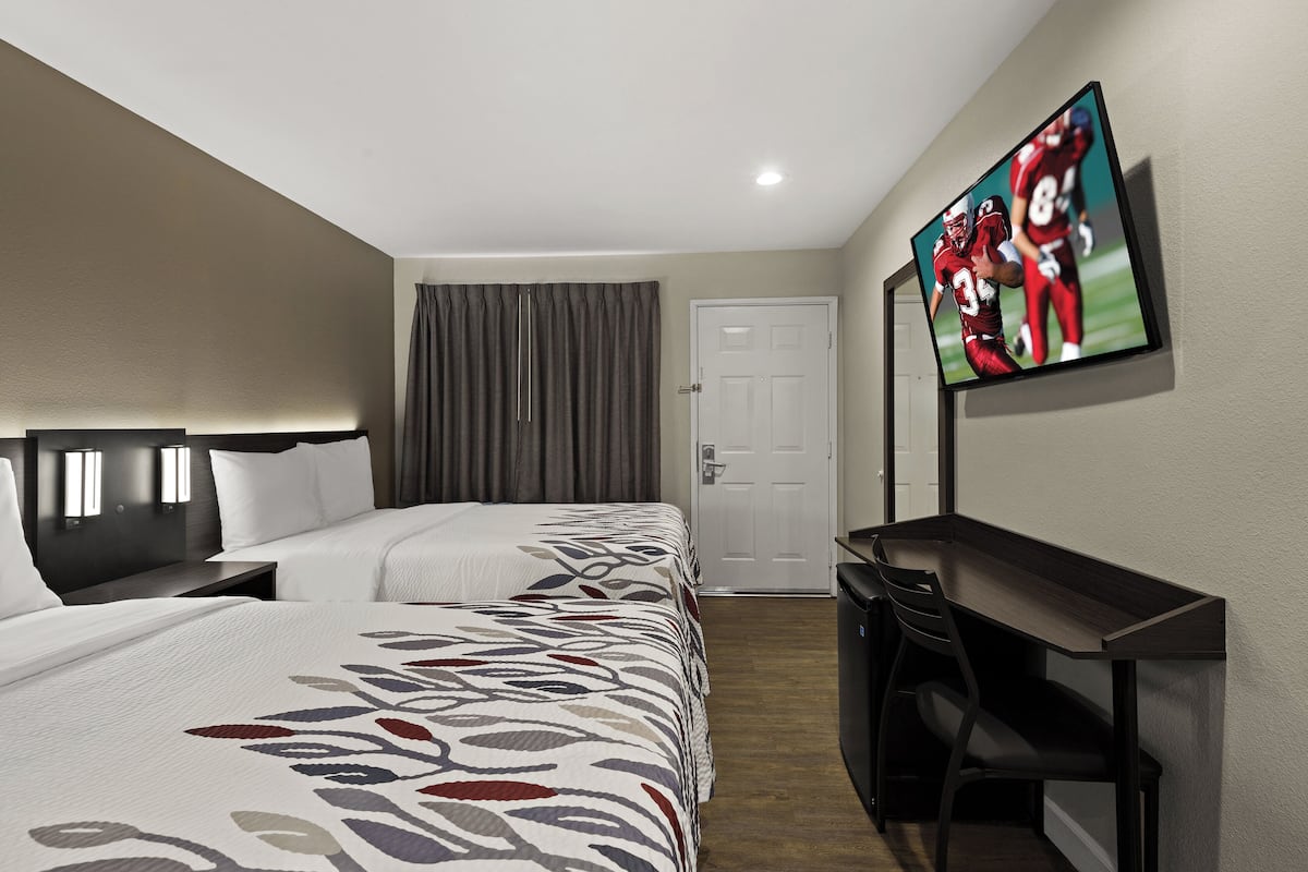 A hotel room with two beds, a desk, a television, and a door.