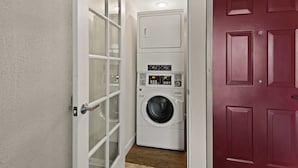 A laundry room with a washing machine and dryer, a door with frosted glass panels, and a red door. - Red Roof Inn Los Angeles - Wilmington, CA (Wilmington)