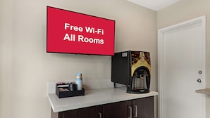 A room with a coffee machine, a stack of cups, and a sign stating "Free Wi-Fi All Rooms".