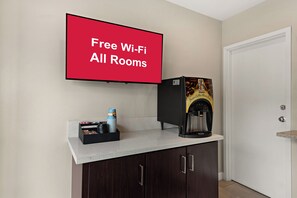 Una habitación con cafetera, una pila de tazas y un cartel que indica 'Free Wi-Fi All Rooms'.