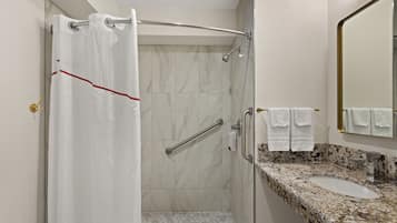 A bathroom with a shower, grab bar, and a sink with a marble countertop.