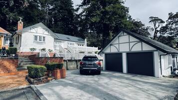 A residential driveway with a car parked in the middle, surrounded by a white house with a garage and a brick wall.
